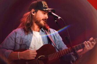 Cory Asbury de boné e camisa jeans tocando violão e cantando no palco durante um show