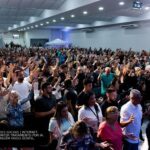 Fiéis evangélicos de mãos erguidas durante culto de adoração em igreja no Brasil