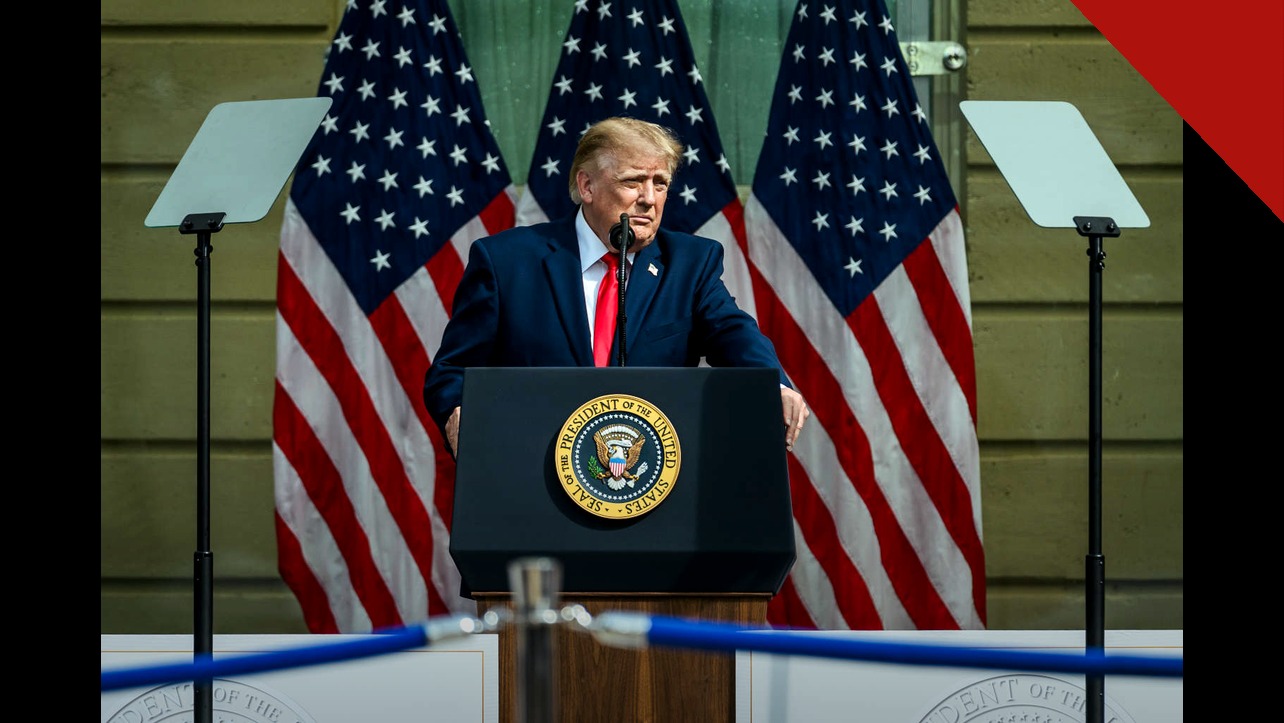 Donald Trump discursa em púlpito presidencial diante de três bandeiras dos Estados Unidos.