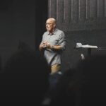 Pastor Ricardo Carvalho, fundador da Igreja Mananciais, pregando no púlpito durante um culto, com a Bíblia aberta ao lado.