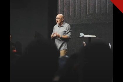 Pastor Ricardo Carvalho, fundador da Igreja Mananciais, pregando no púlpito durante um culto, com a Bíblia aberta ao lado.