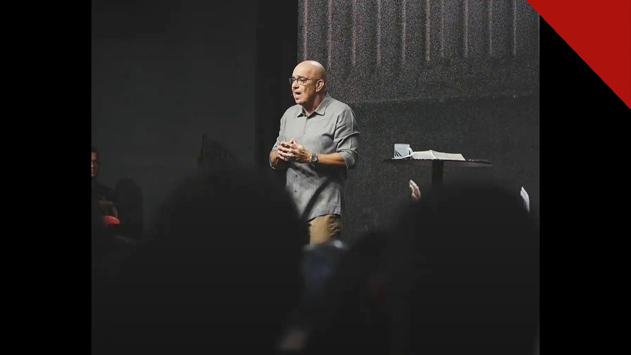 Pastor Ricardo Carvalho, fundador da Igreja Mananciais, pregando no púlpito durante um culto, com a Bíblia aberta ao lado.