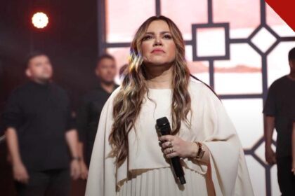A cantora gospel Sarah Farias se apresenta de vestido branco com microfone, sob luzes rosas no palco