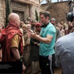 Dallas Jenkins dirige atores caracterizados no set de The Chosen; composição de imagem Hugo Gospel