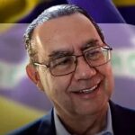 Augusto Cury pede votos para Flávio Bolsonaro: o escritor sorrindo em foto de divulgação, com a bandeira do Brasil ao fundo