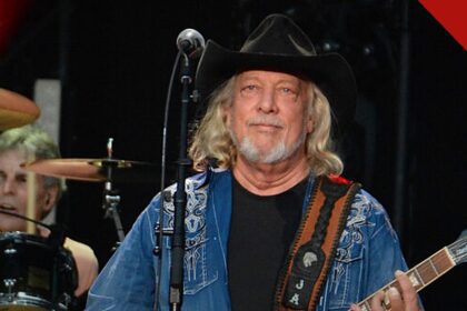 John Anderson morre aos 71 anos: cantor country de chapéu preto e guitarra no palco durante show