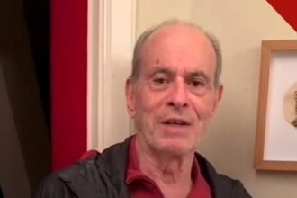 Ney Matogrosso cancela show após cirurgia: cantor de camisa vermelha e jaqueta preta falando em vídeo gravado em casa