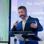 pastor critica fiéis desigrejados: Rick Harrington prega com microfone em conferência cristã na Itália