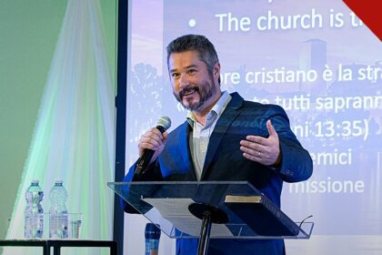 pastor critica fiéis desigrejados: Rick Harrington prega com microfone em conferência cristã na Itália