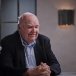 John Lennox exorta cristãos a evangelizar: o matemático de Oxford, de terno escuro e mãos entrelaçadas, conversa durante entrevista
