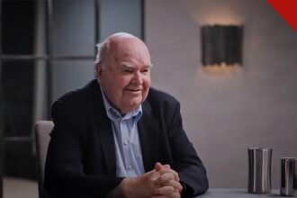 John Lennox exorta cristãos a evangelizar: o matemático de Oxford, de terno escuro e mãos entrelaçadas, conversa durante entrevista