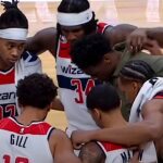 Jogadores do Washington Wizards de cabeça baixa em círculo de oração com Barnes no meio da quadra, em imagem que ilustra como jogadores do Wizards oram com Scottie Barnes após a partida