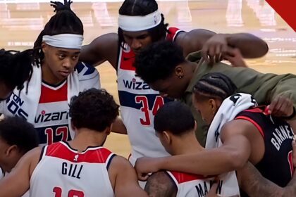 Jogadores do Washington Wizards de cabeça baixa em círculo de oração com Barnes no meio da quadra, em imagem que ilustra como jogadores do Wizards oram com Scottie Barnes após a partida