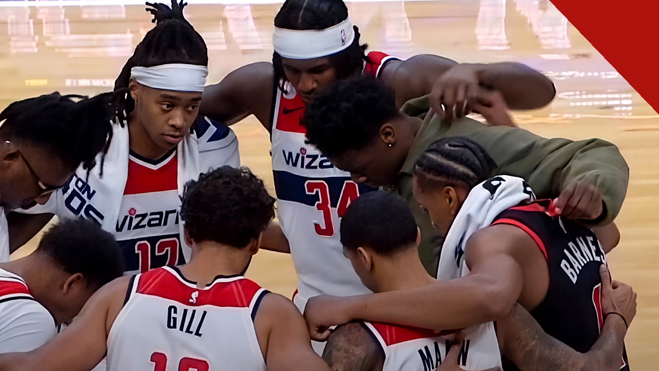 Jogadores do Washington Wizards de cabeça baixa em círculo de oração com Barnes no meio da quadra, em imagem que ilustra como jogadores do Wizards oram com Scottie Barnes após a partida