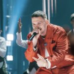Hulvey cancela show: o rapper cristão Hulvey canta com microfone em apresentação, vestindo roupa vermelha, com dançarinos ao fundo