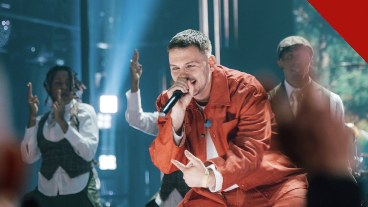Hulvey cancela show: o rapper cristão Hulvey canta com microfone em apresentação, vestindo roupa vermelha, com dançarinos ao fundo