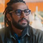 Amaury Lorenzo revela avanço da surdez: o ator como Lucas, personagem da novela Por Você, de dreadlocks e óculos em cena da trama da Globo