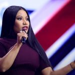 Nicki Minaj em comício com Trump: a rapper falando ao microfone em evento público, de vestido vinho e cabelos longos