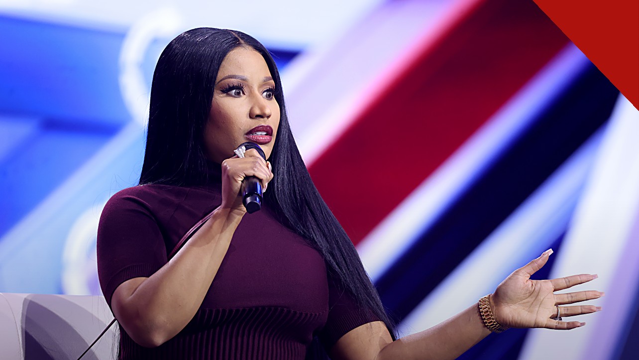 Nicki Minaj em comício com Trump: a rapper falando ao microfone em evento público, de vestido vinho e cabelos longos