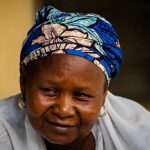 mãe cristã presa na Nigéria: Rhoda Jatau, de lenço azul estampado e véu branco, sorrindo ao lado do advogado Sean Nelson, da ADF International