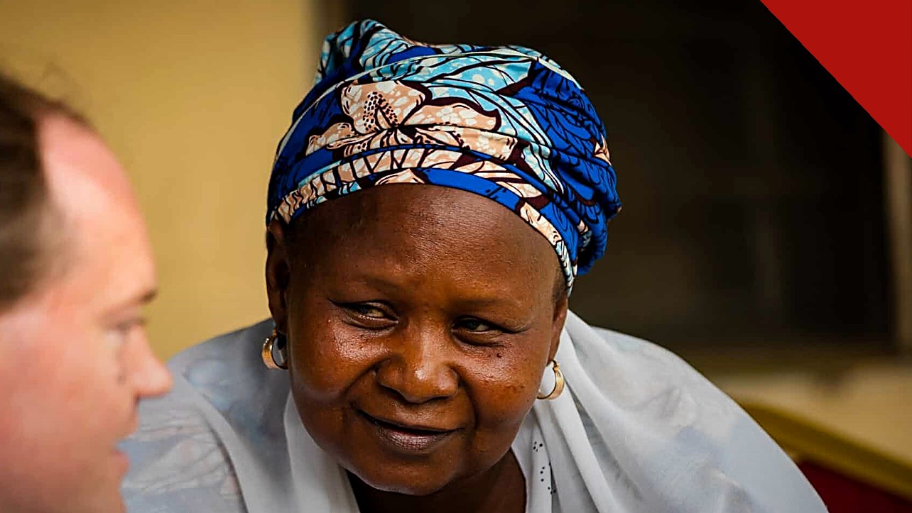 mãe cristã presa na Nigéria: Rhoda Jatau, de lenço azul estampado e véu branco, sorrindo ao lado do advogado Sean Nelson, da ADF International