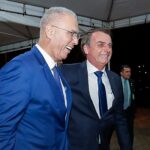 grupo de oração visita Bolsonaro: Jair Bolsonaro falando ao microfone em evento oficial, com bandeira ao fundo