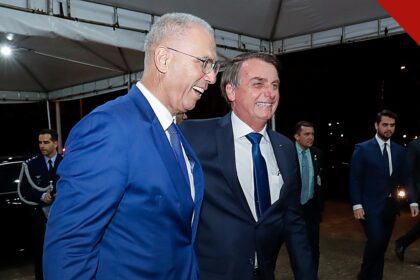 grupo de oração visita Bolsonaro: Jair Bolsonaro falando ao microfone em evento oficial, com bandeira ao fundo