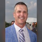 Harbaugh agradece a Deus por vitória: retrato de John Harbaugh sorrindo, de paletó azul e gravata listrada, em foto de arquivo