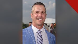Harbaugh agradece a Deus por vitória: retrato de John Harbaugh sorrindo, de paletó azul e gravata listrada, em foto de arquivo