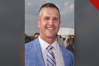 Harbaugh agradece a Deus por vitória: retrato de John Harbaugh sorrindo, de paletó azul e gravata listrada, em foto de arquivo