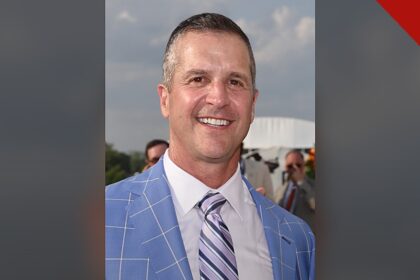 Harbaugh agradece a Deus por vitória: retrato de John Harbaugh sorrindo, de paletó azul e gravata listrada, em foto de arquivo