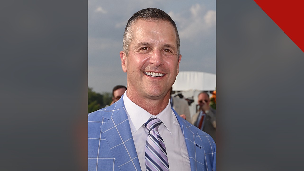 Harbaugh agradece a Deus por vitória: retrato de John Harbaugh sorrindo, de paletó azul e gravata listrada, em foto de arquivo