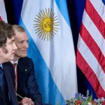 Milei vai à inauguração de igreja evangélica: presidente argentino de perfil, com as bandeiras da Argentina e dos Estados Unidos ao fundo