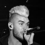 Colton Dixon fala da música Bones: cantor de moicano claro cantando ao microfone em show, em preto e branco