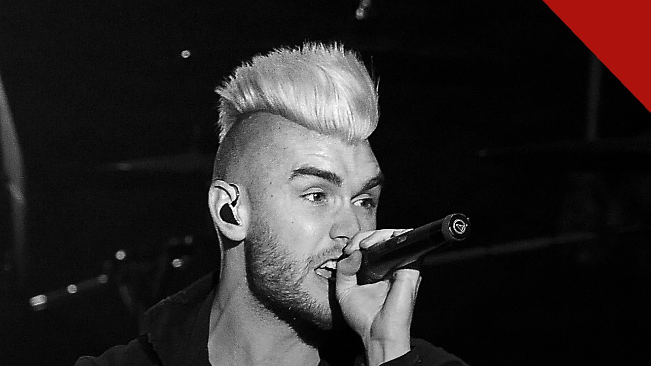 Colton Dixon fala da música Bones: cantor de moicano claro cantando ao microfone em show, em preto e branco