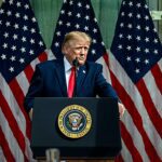 Conselho de Paz de Trump nomeia ex oficial de Biden é a decisão do Conselho, e a imagem mostra o presidente Donald Trump falando em púlpito oficial com bandeiras dos Estados Unidos