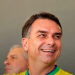 Flávio Bolsonaro deixou o Brasil rumo aos Estados Unidos, e a imagem mostra o senador Flávio Bolsonaro sorrindo com a camisa da seleção brasileira