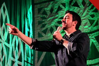 relato de Padre Fábio de Melo volta a repercutir nas redes sociais, e a imagem mostra o Padre Fábio de Melo cantando e apontando em show com luz verde