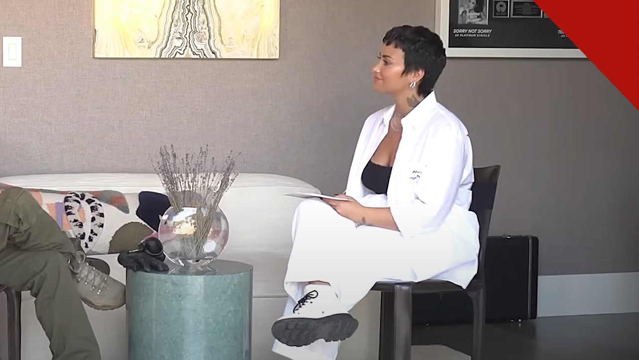 Demi Lovato é hospitalizada após reação alérgica e recebe alta, e a imagem mostra a cantora Demi Lovato sentada de roupa branca em entrevista
