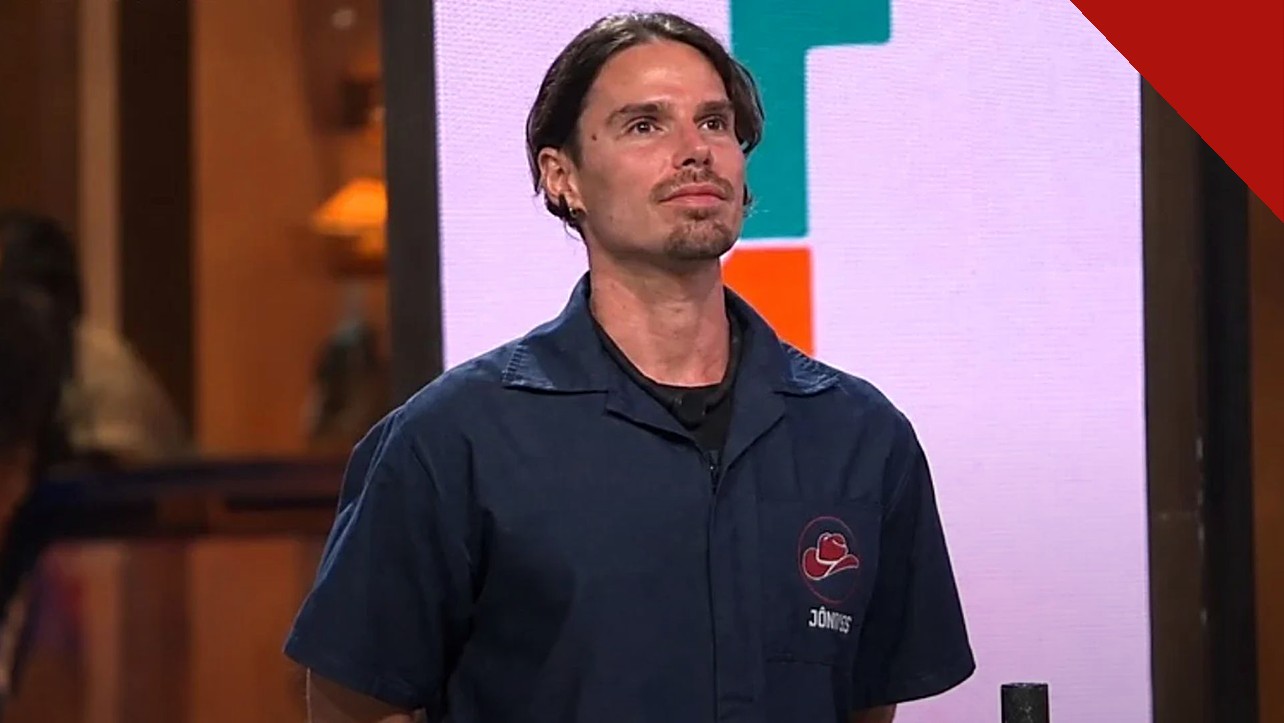 Jônatas Faro explica desistência de A Fazenda 18 no reality da Record, e a imagem mostra o ator Jônatas Faro com o uniforme do programa A Fazenda, de camisa azul com o nome bordado