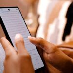 app da Bíblia atinge 1,1 milhão de usuários diários no Brasil todos os dias, e a imagem mostra mãos segurando um celular com o texto bíblico aberto no aplicativo