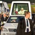 exposição de papamóveis históricos no Vaticano, e a imagem mostra o Papa Bento XVI acenando do papamóvel Mercedes-Benz com cúpula transparente, cercado por seguranças