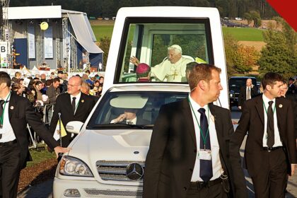 exposição de papamóveis históricos no Vaticano, e a imagem mostra o Papa Bento XVI acenando do papamóvel Mercedes-Benz com cúpula transparente, cercado por seguranças