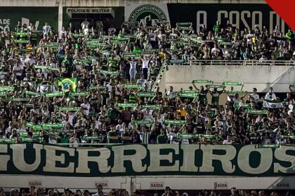 Jakson Follmann relembra como soube das mortes dos companheiros, e a imagem mostra a torcida da Chapecoense com cachecóis e a faixa Guerreiros em tributo na Arena Condá