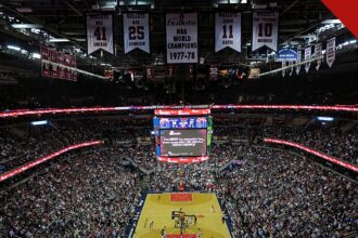 Ernie Johnson deixa o Inside the NBA após 3 décadas, e a imagem mostra o interior de uma arena da NBA lotada, com a quadra de basquete ao centro e faixas de campeões no teto