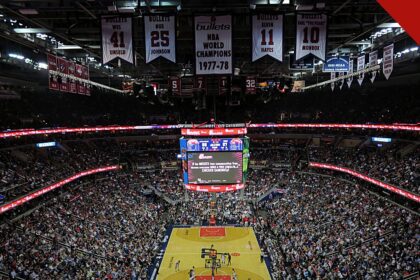 Ernie Johnson deixa o Inside the NBA após 3 décadas, e a imagem mostra o interior de uma arena da NBA lotada, com a quadra de basquete ao centro e faixas de campeões no teto