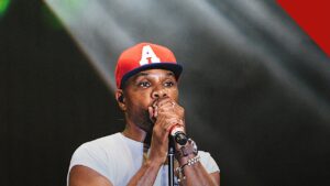 Kirk Franklin lança álbum duplo como resposta aos críticos, e a imagem mostra Kirk Franklin cantando em um palco, de boné vermelho e camiseta branca, segurando um microfone com as duas mãos