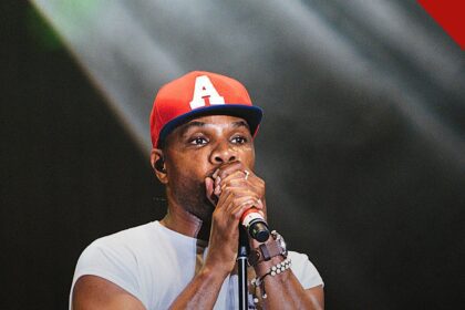 Kirk Franklin lança álbum duplo como resposta aos críticos, e a imagem mostra Kirk Franklin cantando em um palco, de boné vermelho e camiseta branca, segurando um microfone com as duas mãos