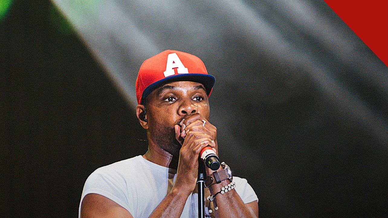 Kirk Franklin lança álbum duplo como resposta aos críticos, e a imagem mostra Kirk Franklin cantando em um palco, de boné vermelho e camiseta branca, segurando um microfone com as duas mãos