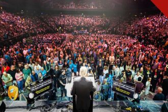 Franklin Graham vê sinais de avivamento: o evangelista de costas no púlpito diante de mais de 10 mil pessoas na arena de Manchester, na turnê God Loves You